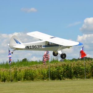 A small white plane flying over some grass