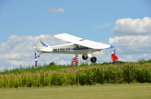 A small white plane flying over some grass